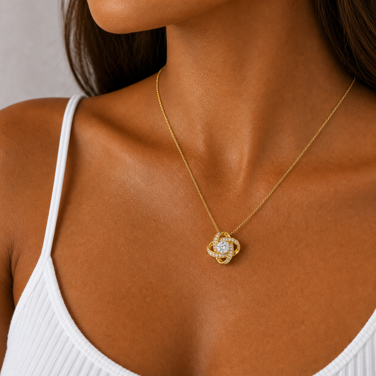 Close-up of the yellow gold love knot pendant worn with a white top